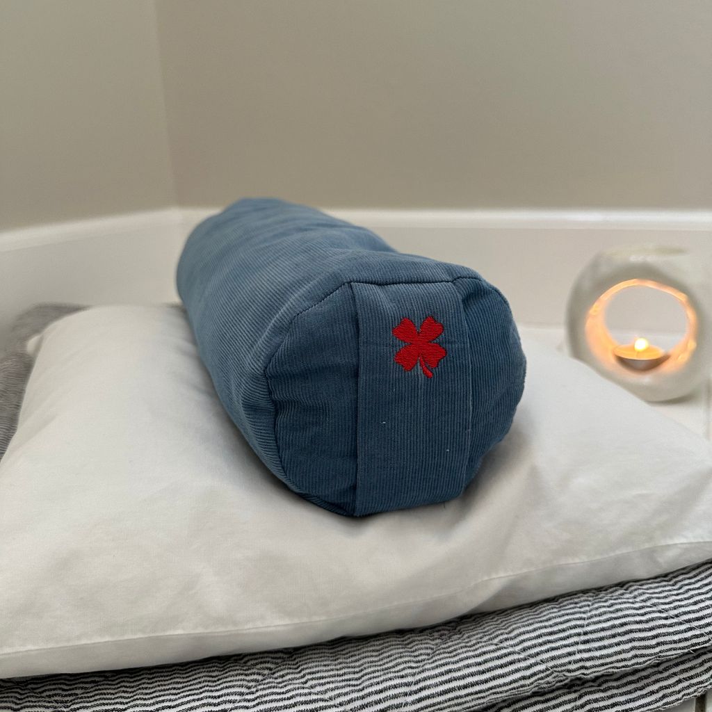 Mini yogabolster med firkløver på pude med stearinlys ved siden af 